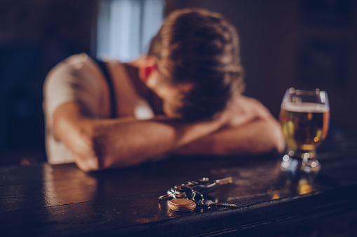 One man, sitting at the bar counter alone, he has drinking problems.