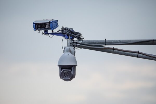 A speed control and traffic monitoring camera is installed above the road on metal structures, against the sky.